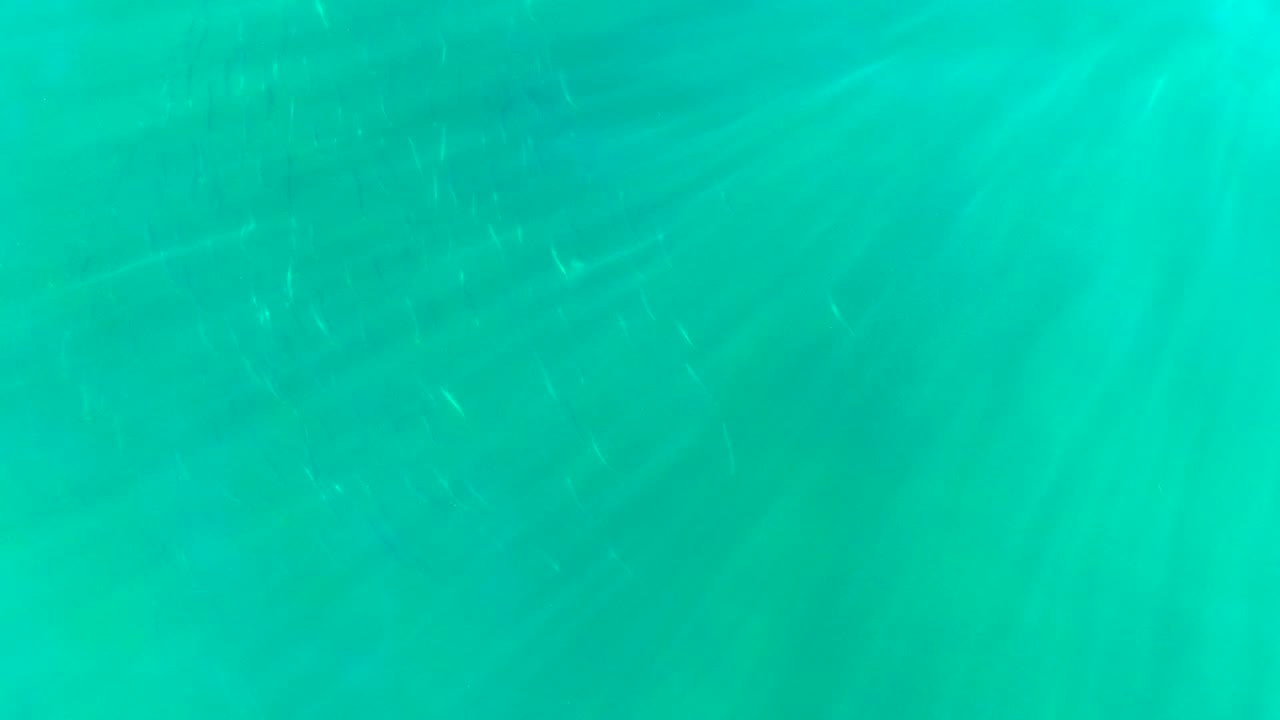 Underwater turquoise frame from La Bocana with a brighter glow near the surface and faint refraction lines, with no visible people.