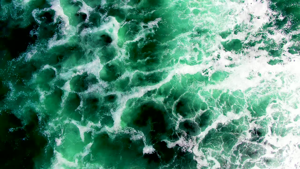 Overhead view of green ocean water at La Bocana with white foam spreading across darker patches and no visible people.