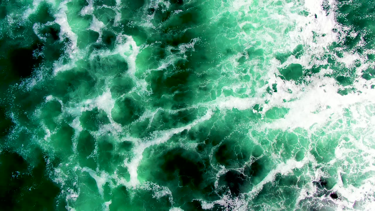 Aerial frame of La Bocana ocean water with white foam curling through emerald and dark green patches, with no visible people.