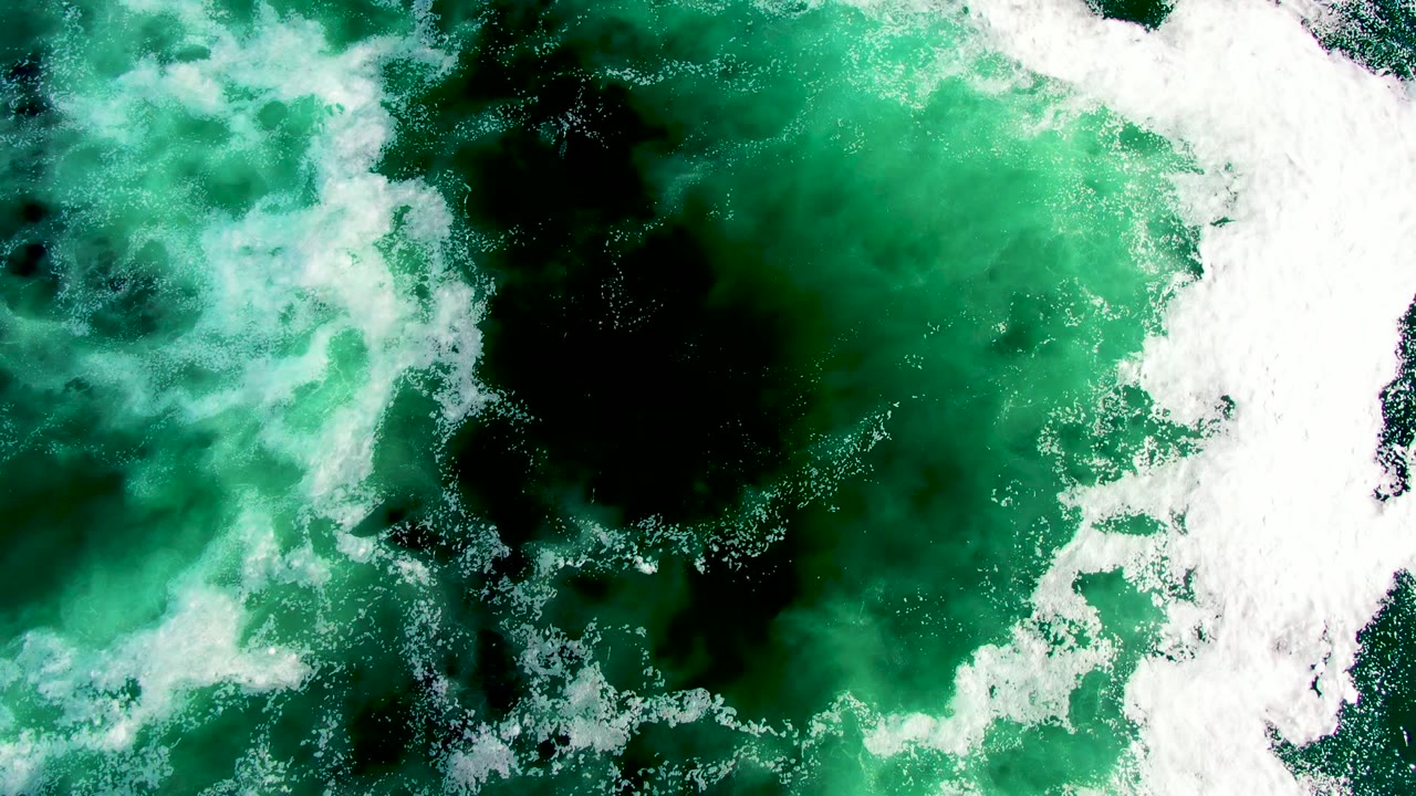 Green surf churns around a large dark patch with white foam on the right.