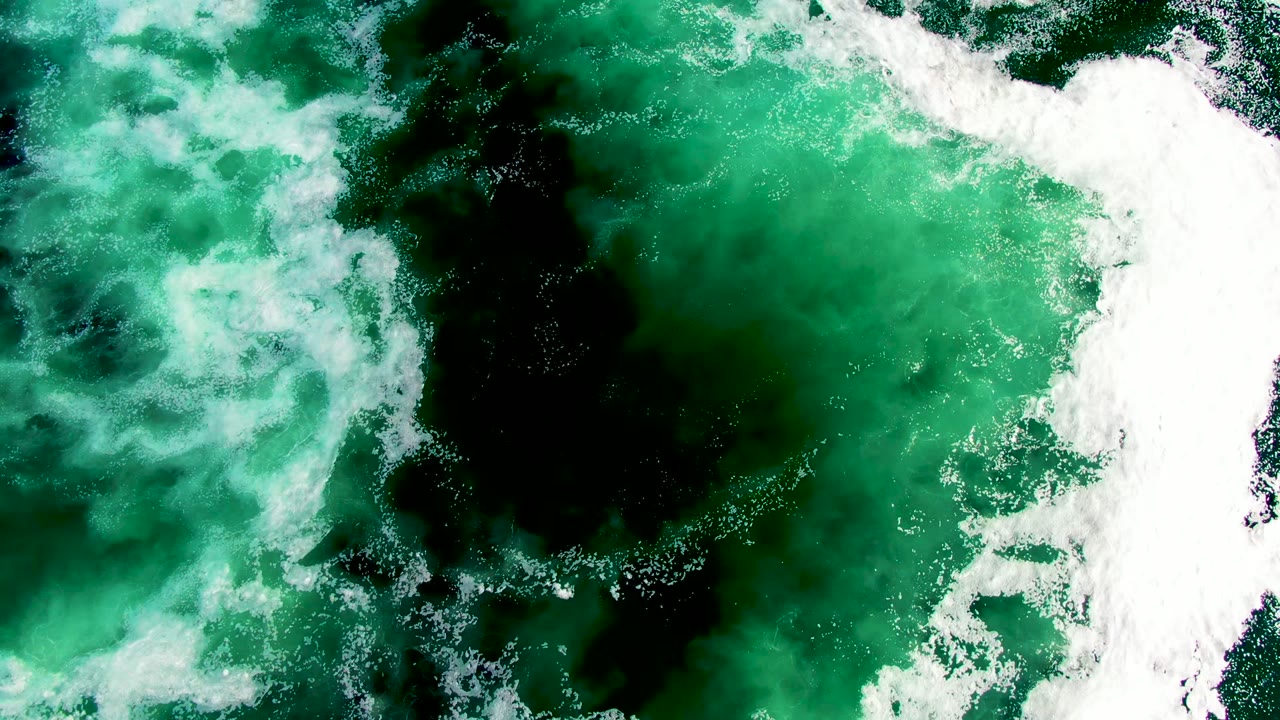 White foam crosses the upper right of green ocean water at La Bocana, Baja California Sur, with a dark central patch and scattered bubbles below, no visible people.
