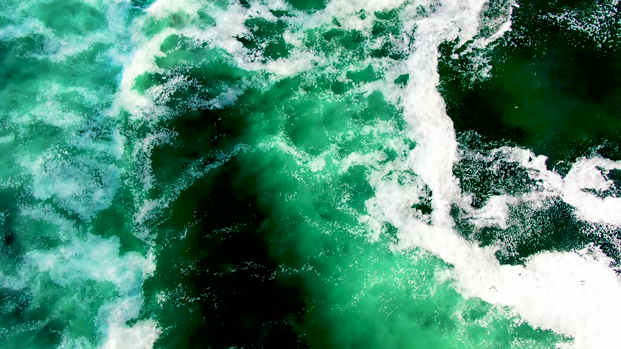 At 0:02, the La Bocana overhead frame shows turbulent white foam bands over green ocean water, with darker submerged areas and no visible people.