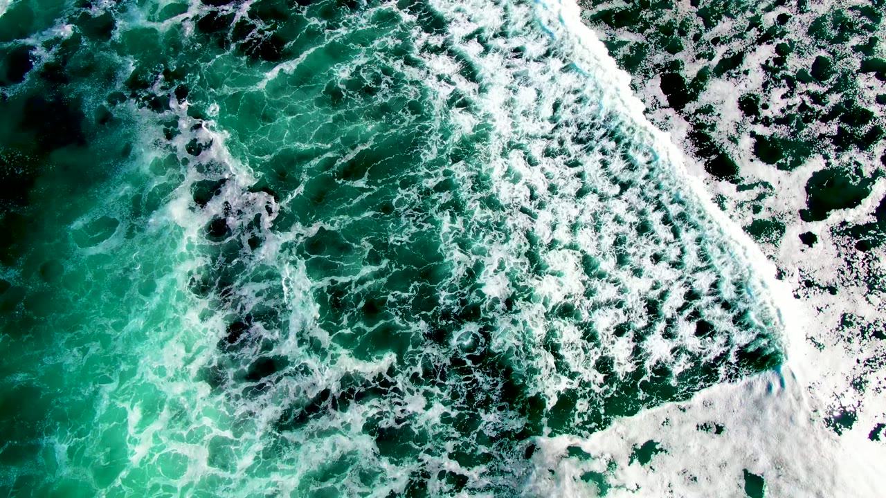 Top-down La Bocana surf frame with white foam gathering over dark underwater areas and bright turquoise water, with no visible people.