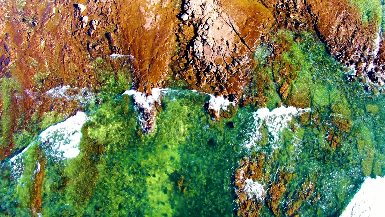 White foam spreads across green water beside jagged rocks.