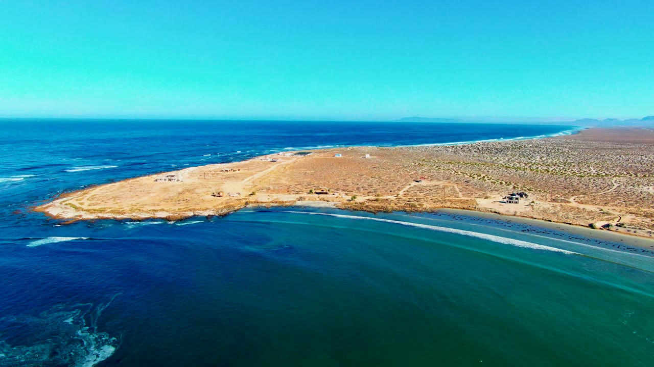Drone view of a curved beach with waves wrapping along a sandy point.