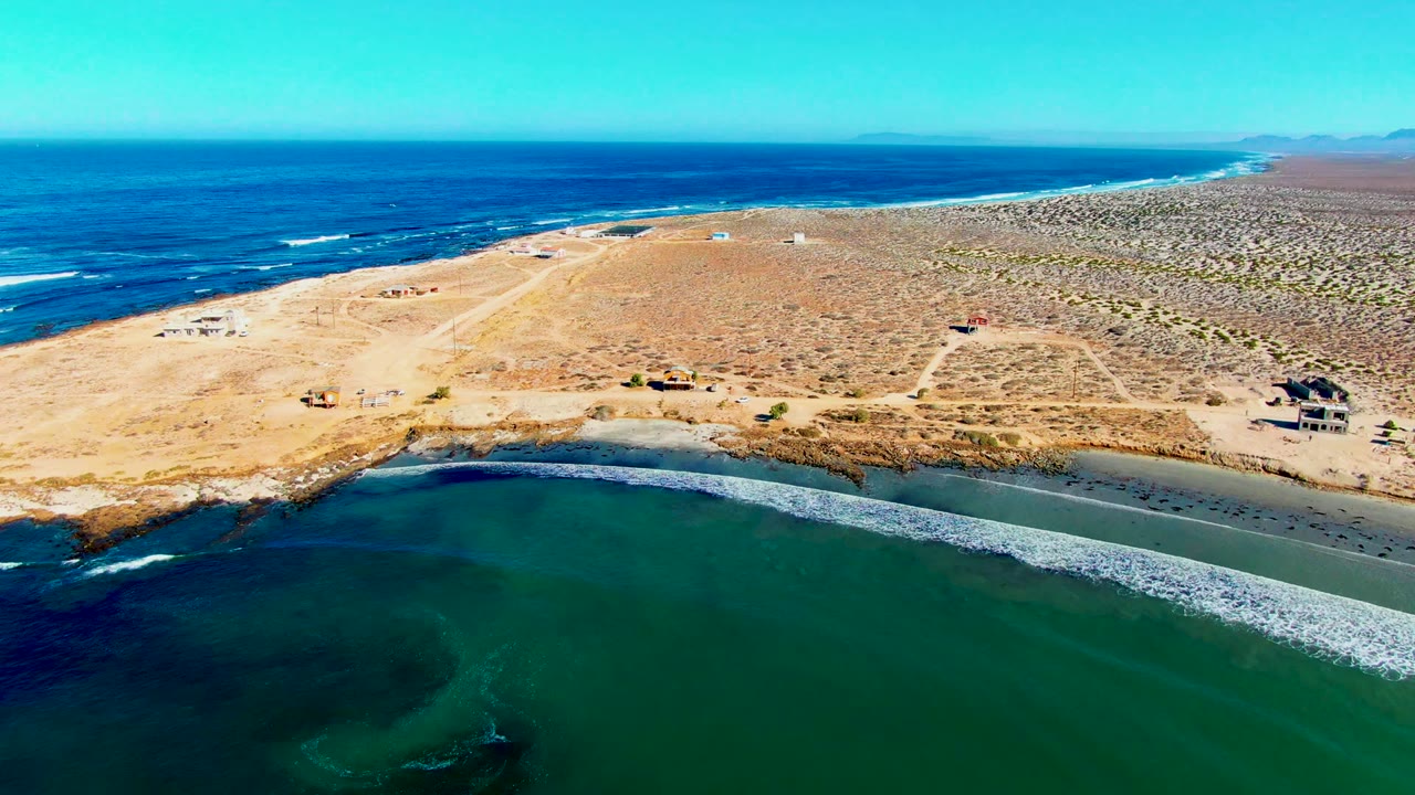 Drone view over green inlet water, sandy beach, and dry coastal land.