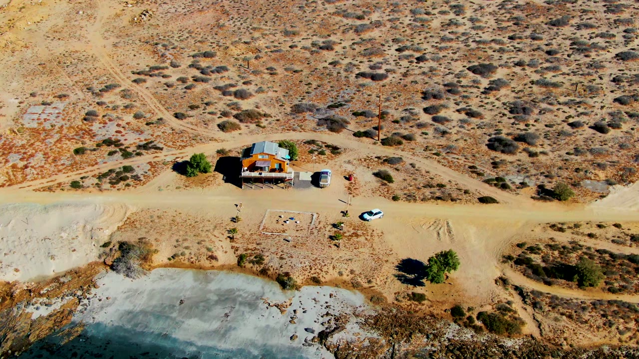 Aerial view of a small desert house, road, car, and water edge.