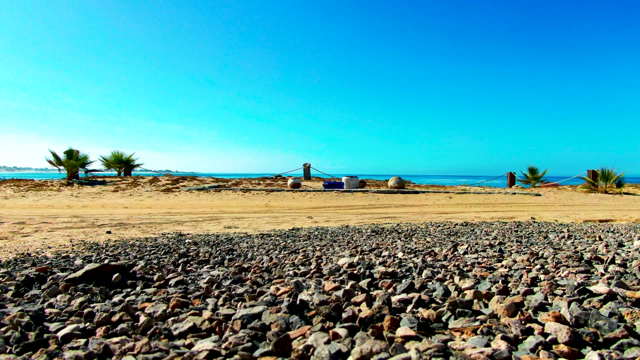 Rocky beach foreground and sandy shore beside a calm blue ocean.