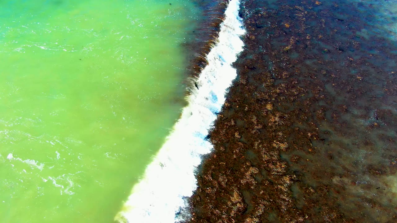 The aerial view shows a stronger white foam band running beside dark brown shallows while green water fills the left side of the La Bocana frame, with no visible people.