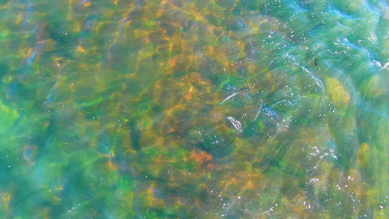 Rippling green-blue water with submerged rocks and bubbles