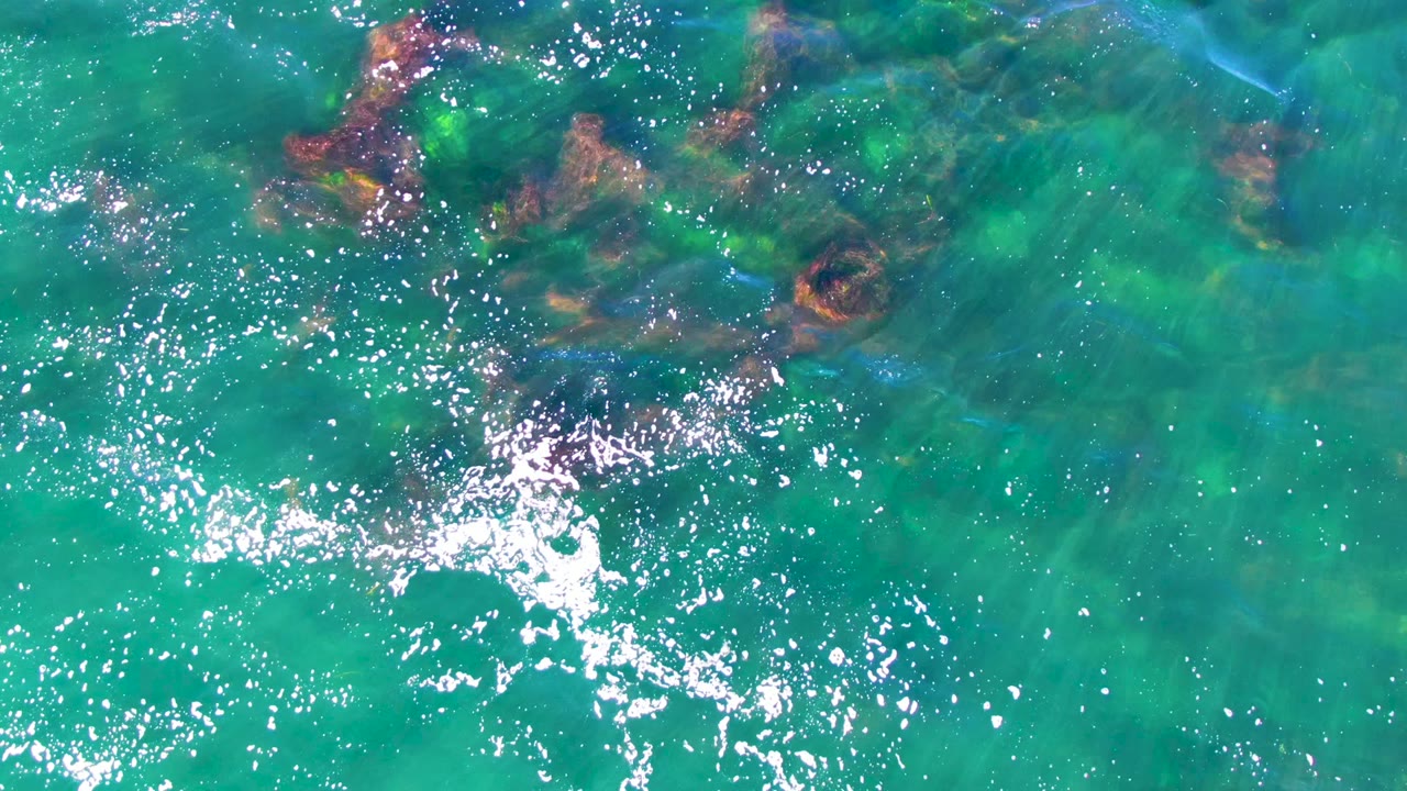 Clear green-blue water with scattered underwater rocks and white glare.
