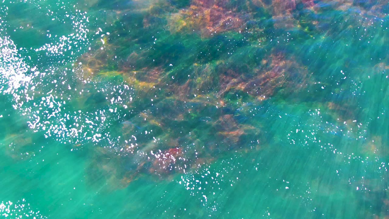 Clear green-blue water with submerged rocks and scattered bubbles.