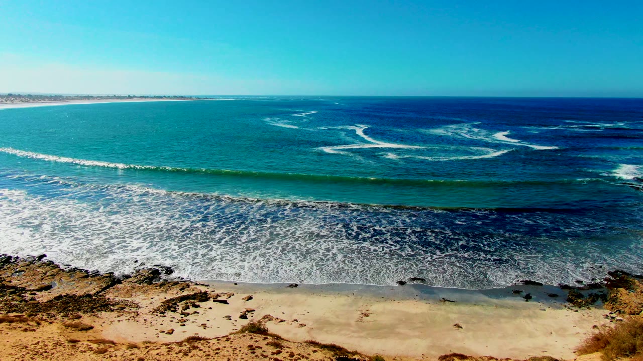 White surf spreading across shallow water below a clear blue horizon