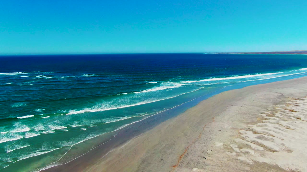 White surf bands angle toward pale sand beside deep blue water.