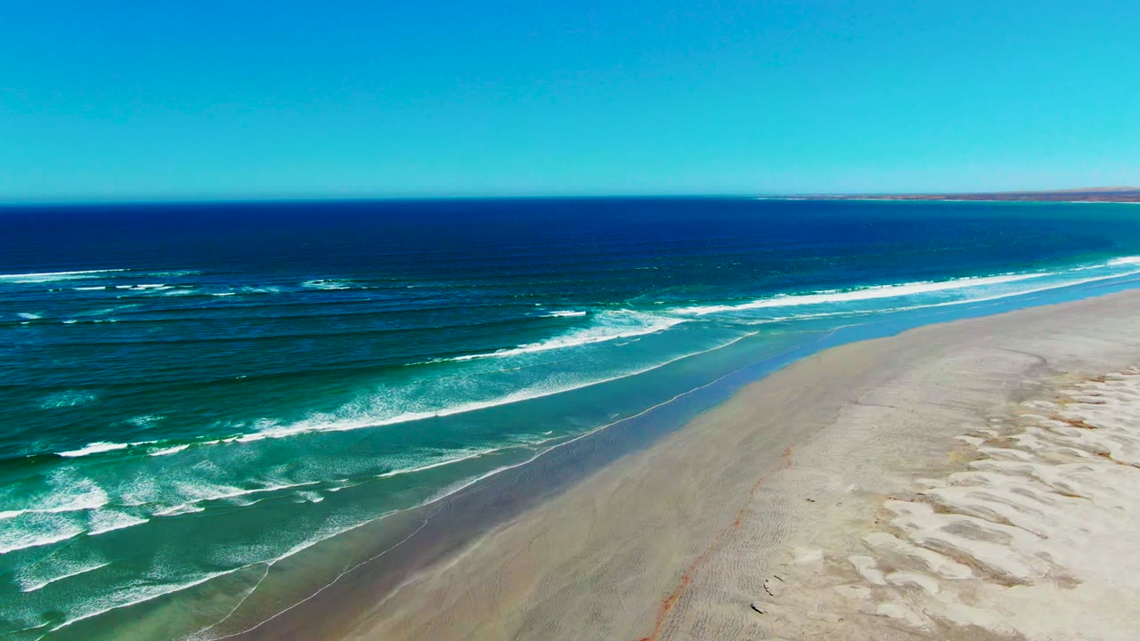 Foamy waves advance in parallel lines toward the broad empty sand at La Bocana, with the ocean filling the left half and no visible people.