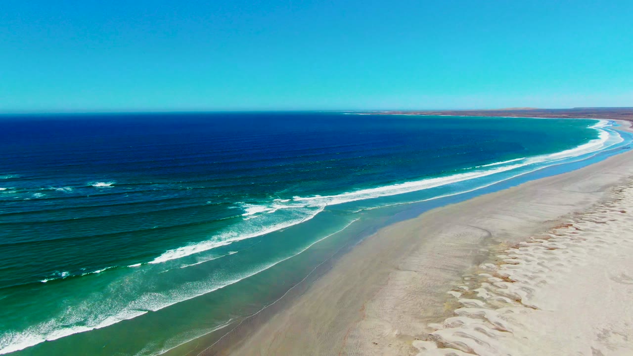 Aerial view along the La Bocana coast with a long curve of sand, blue ocean to the left, foamy breakers near shore, and no visible people.