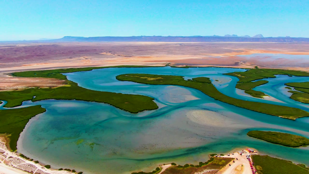 Drone view over blue-green water channels, sandbars, and low desert horizon.