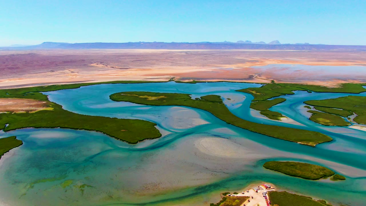 Aerial view of winding blue water channels, green islands, sandbars, and desert horizon.