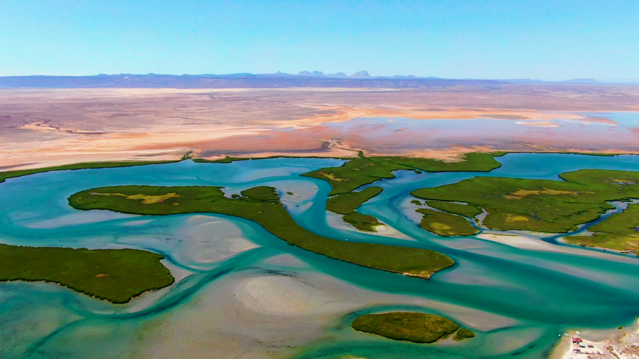Drone view of green islands and turquoise channels beside sandy desert.