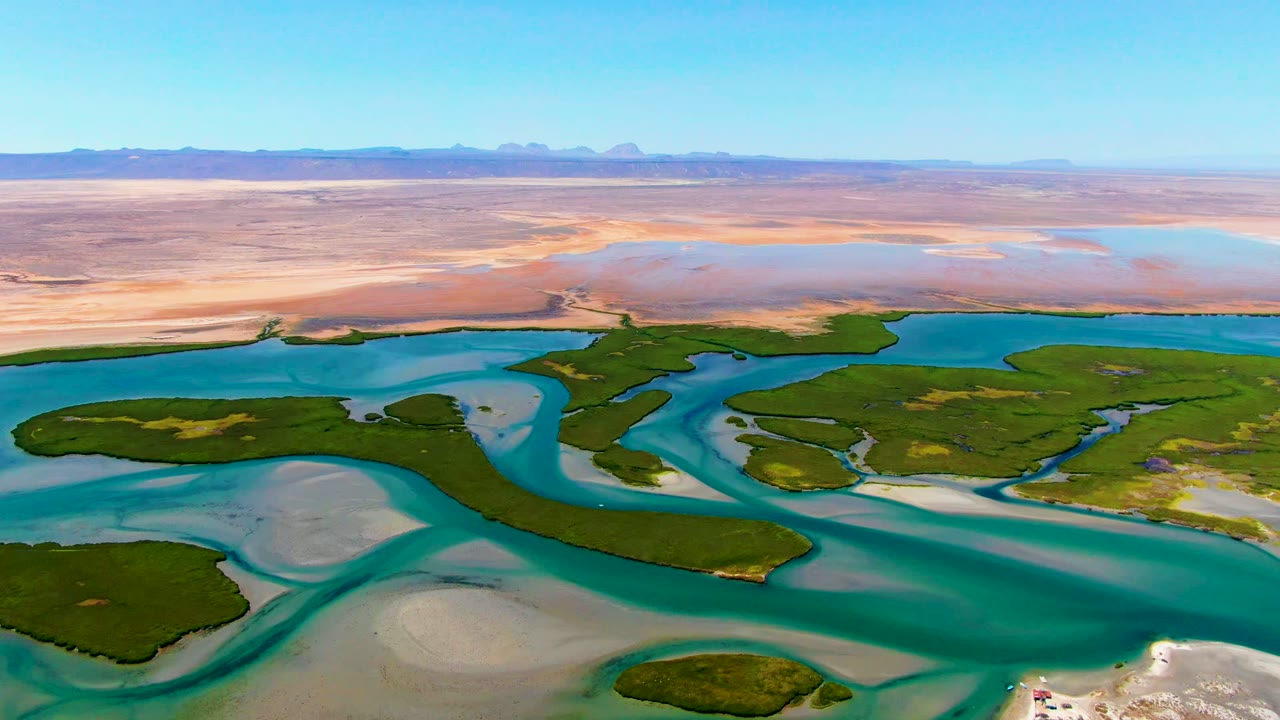Wide drone view of blue water splitting around green islands and pale sand.