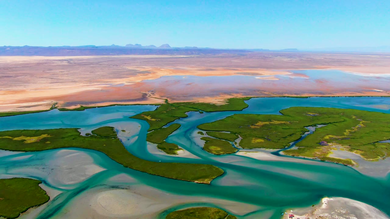 Aerial view in La Bocana, Baja California Sur with green wetland shapes bordered by turquoise water, dry sandy flats across the background, and no visible people.