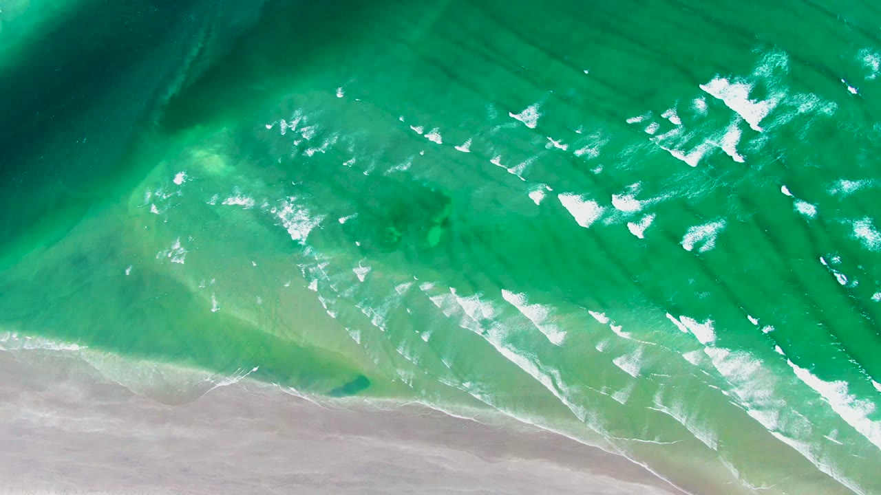 Top-down La Bocana coastal view with darker green water at the upper left, turquoise shallows through the center, white breaking surf, and no visible people.