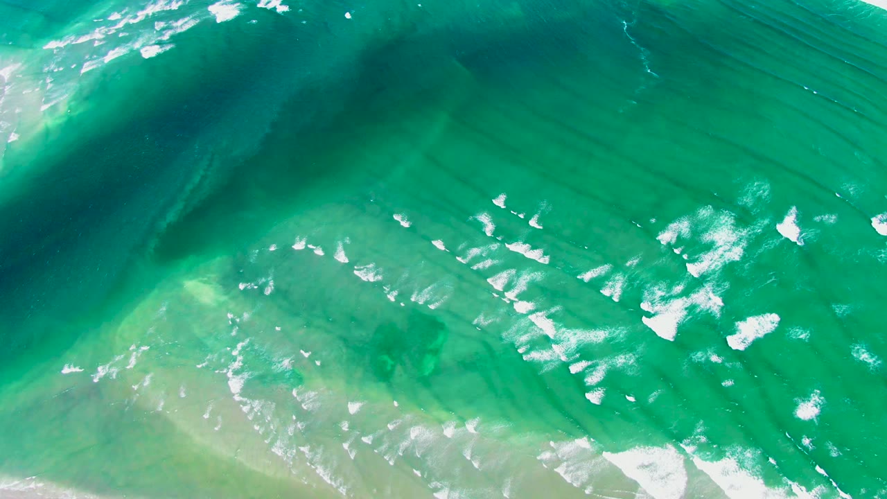 Overhead view of turquoise and green ocean water at La Bocana with white foam breaking across the surface and no visible people.