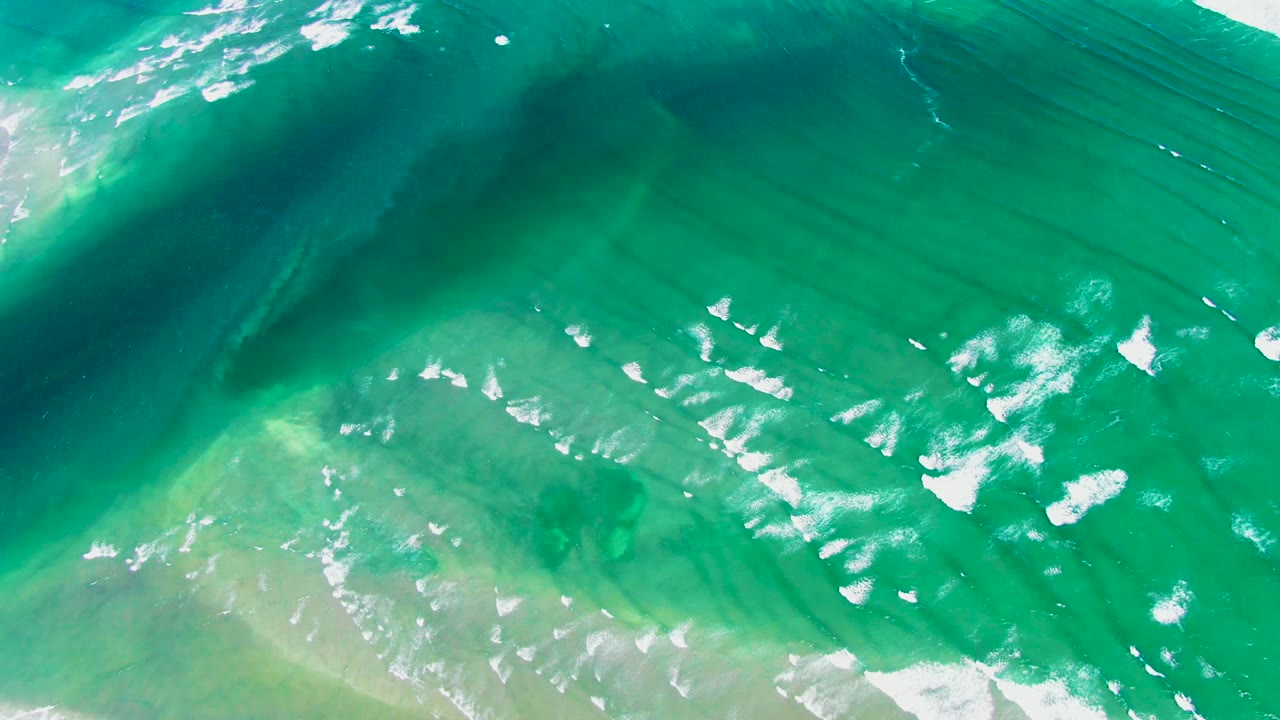 Aerial surf foam drifting over green blue water.