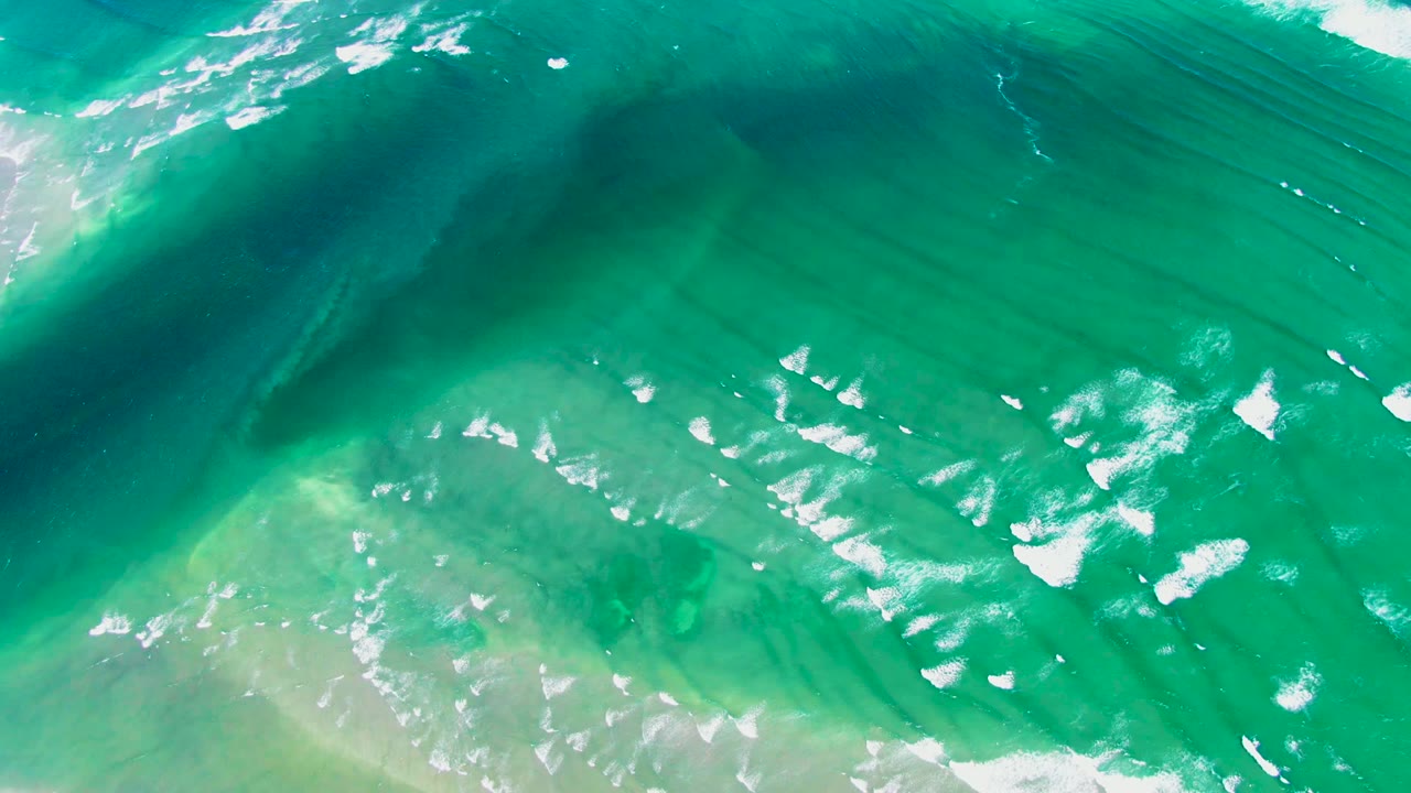 Top-down La Bocana ocean view with a wave break near the upper edge, pale shallow water below, and no visible people.