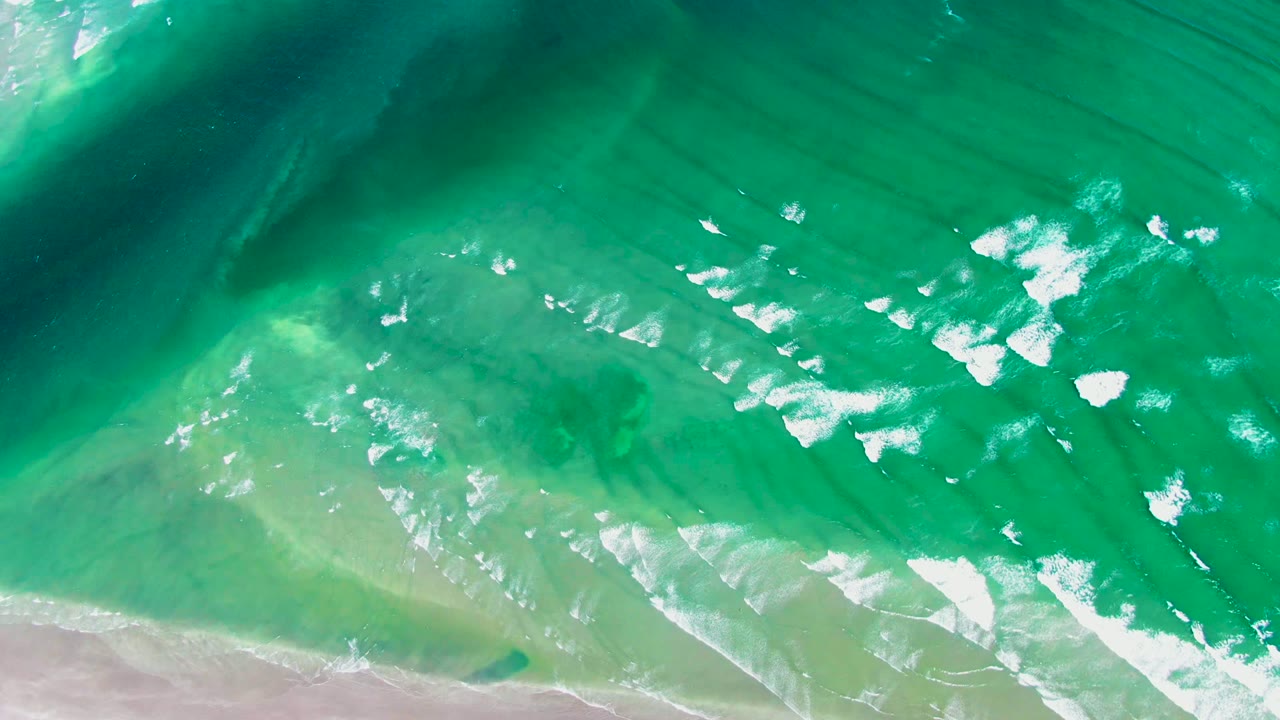 White foam streaks spreading across turquoise shallow water