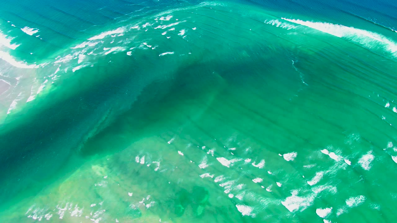 Curving green-blue wave face with foam streaks in sunlight.
