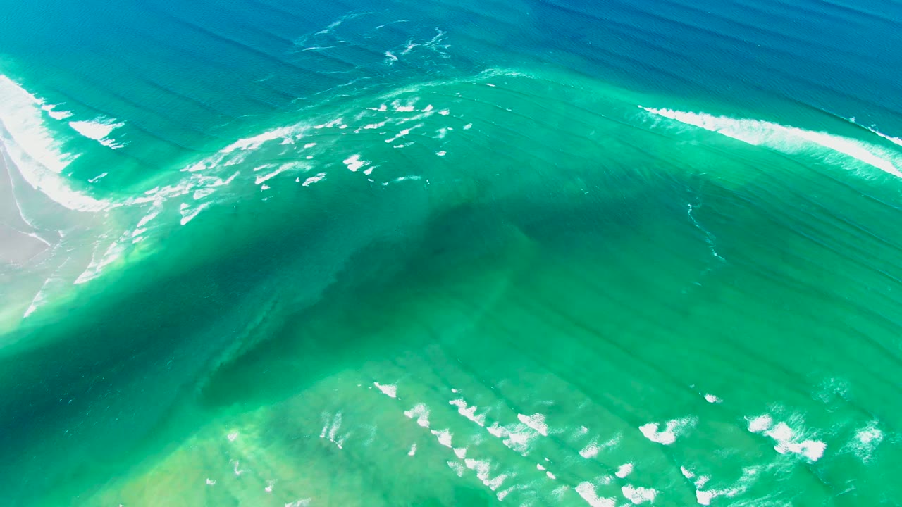 Aerial view of turquoise water, white foam, and a pale sandy edge at La Bocana, Baja California Sur, with no visible people.