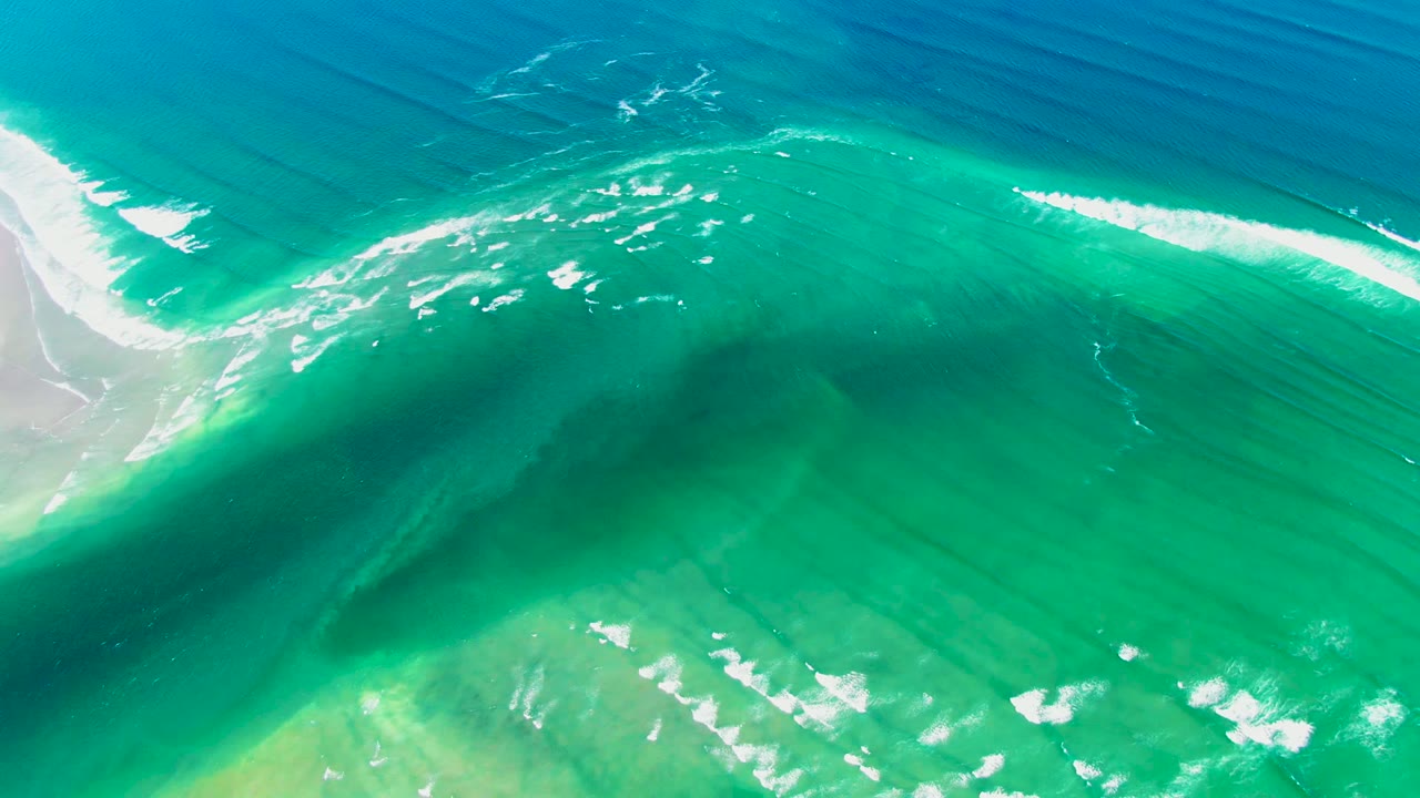 White wave foam crossing clear green-blue coastal water
