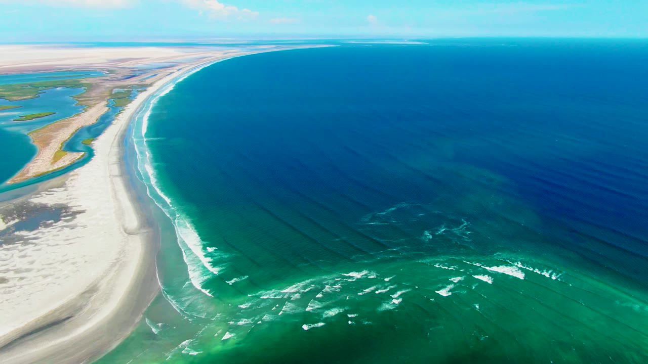 Aerial view over La Bocana, Baja California Sur showing a sandy beach curving along turquoise and deep blue ocean with white surf and no visible people.