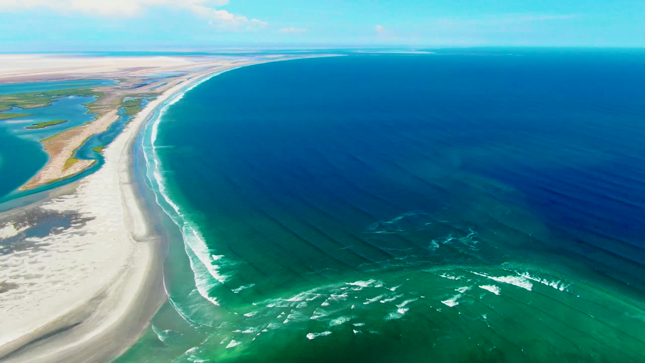High aerial coastline with sand flats, turquoise shallows, and deep blue ocean