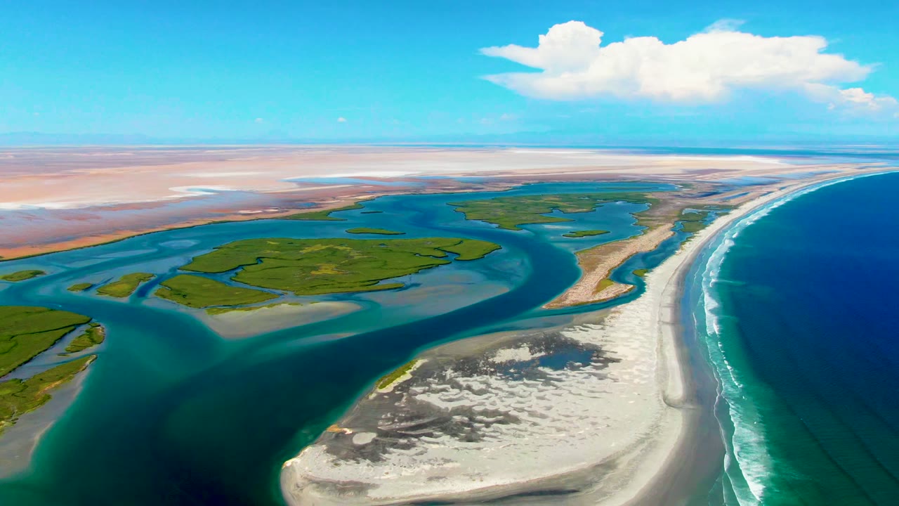 Aerial coastal lagoon with green islands, channels, beach, and ocean waves.