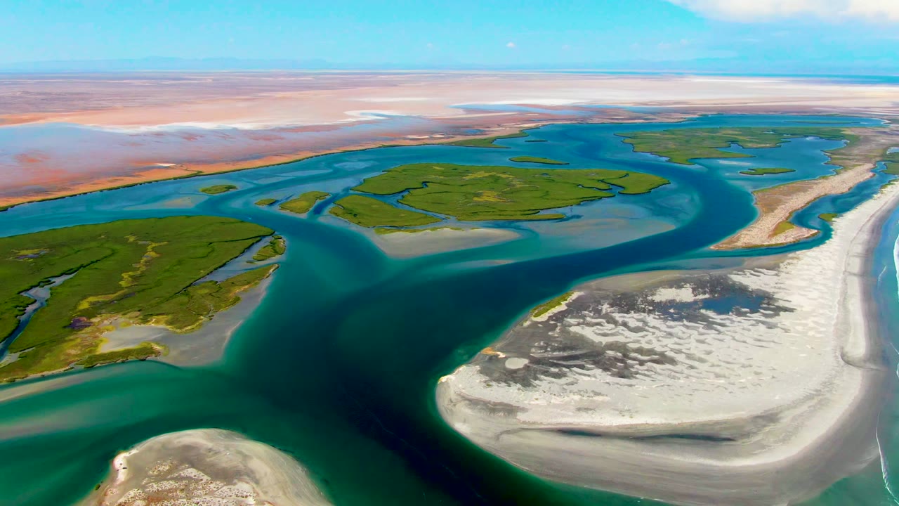 Opening aerial frame over La Bocana, Baja California Sur, showing blue-green water wrapping around green delta islands and pale sandy banks, with no visible people.