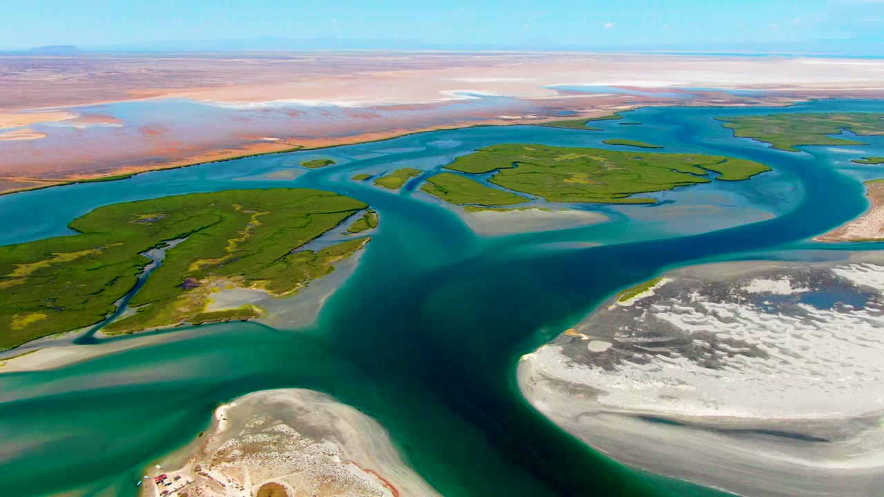 Drone view of teal water curving past sandy flats and vegetation