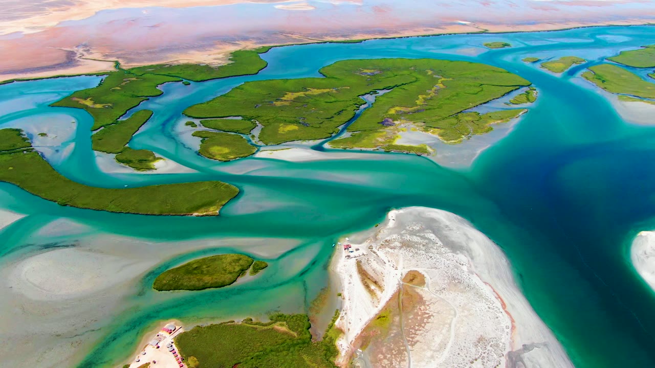 Drone view of lagoon islands and shallow turquoise water beside white sand.