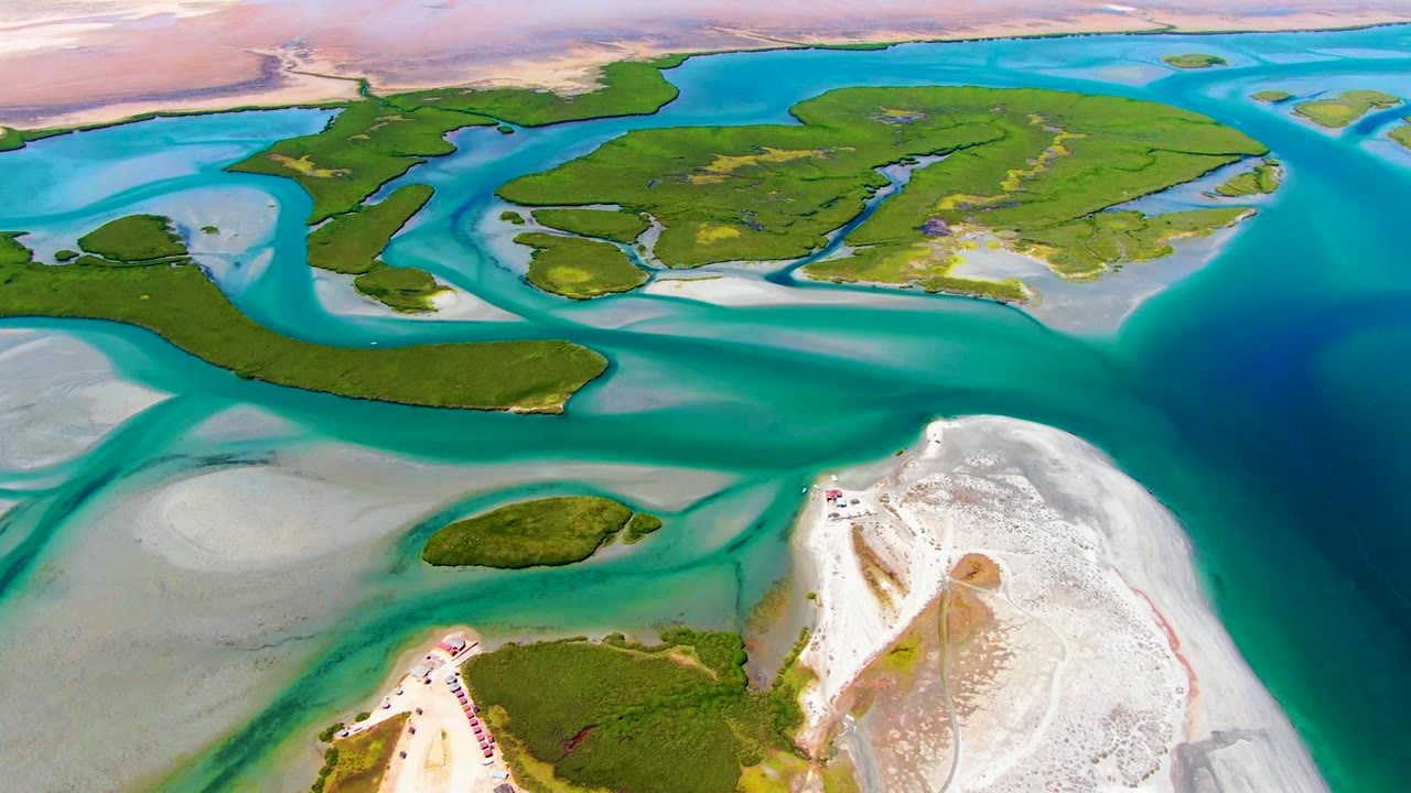 High oblique aerial at La Bocana with a white sandbar in the lower right, green island vegetation across the middle, layered turquoise and blue water, and no visible people.