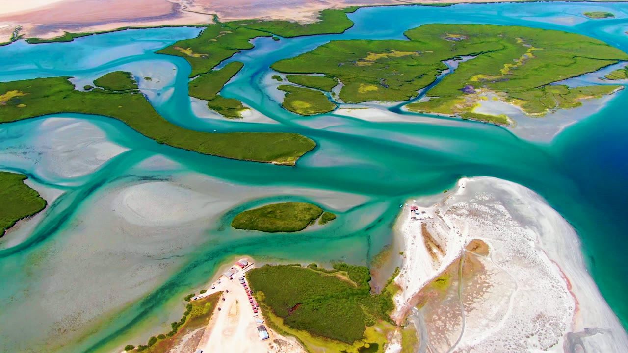 Drone view of bright blue lagoon water, green island patches, and exposed sandy shore.