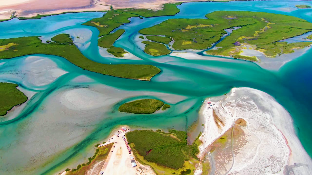 At 0:02, a wide drone frame over La Bocana shows branching turquoise tidal channels, low green islands, white sand shoreline, and no visible people.
