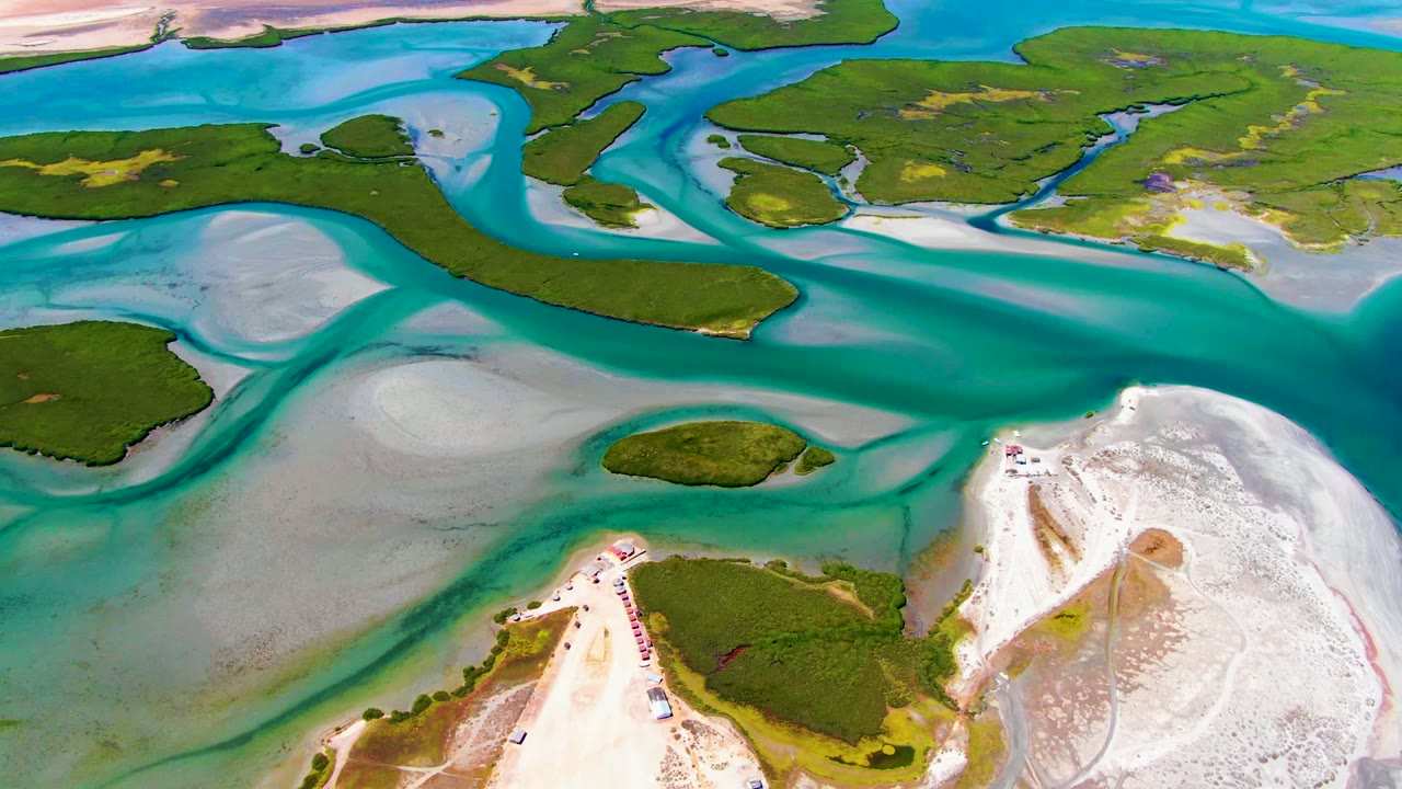 Drone view of shallow blue-green water between islands and a white sand shore.