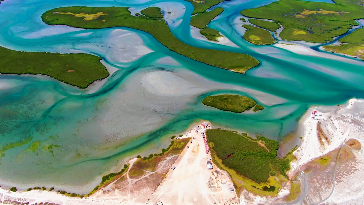 Opening aerial frame over La Bocana, Baja California Sur, with turquoise tidal channels wrapping around green islands, pale sand flats, and no visible people.