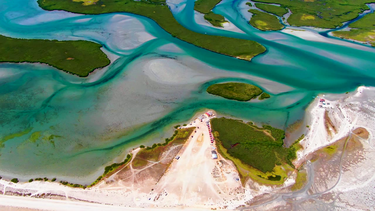 Overhead coastal view with a sandy spit, green vegetation, and turquoise water.