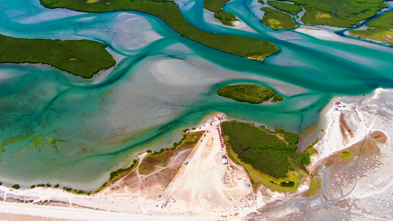 Aerial frame at 0:02 in La Bocana showing a broad turquoise channel, exposed sand flats, low green islets, and no visible people.