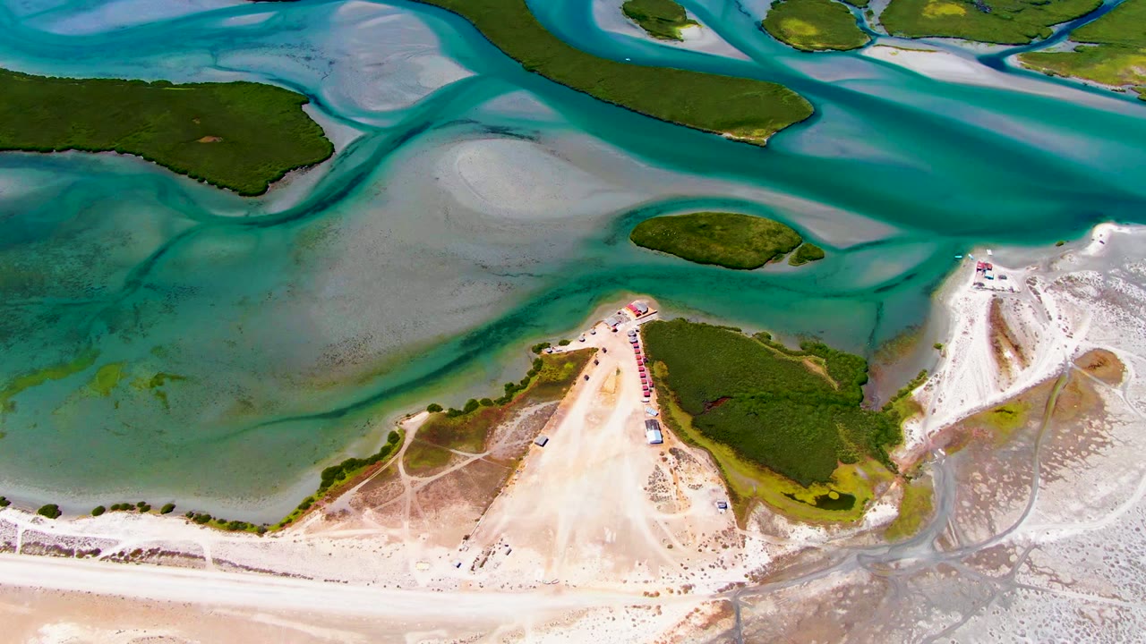 Overhead coastal shallows with green islands, sand flats, and curving blue-green water.