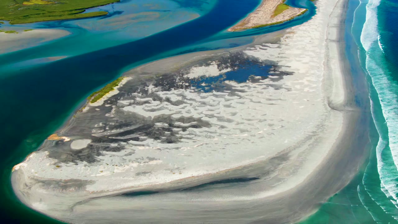 Aerial frame over La Bocana, Baja California Sur, showing a white sandbar between a dark blue river channel and turquoise ocean surf with no visible people.