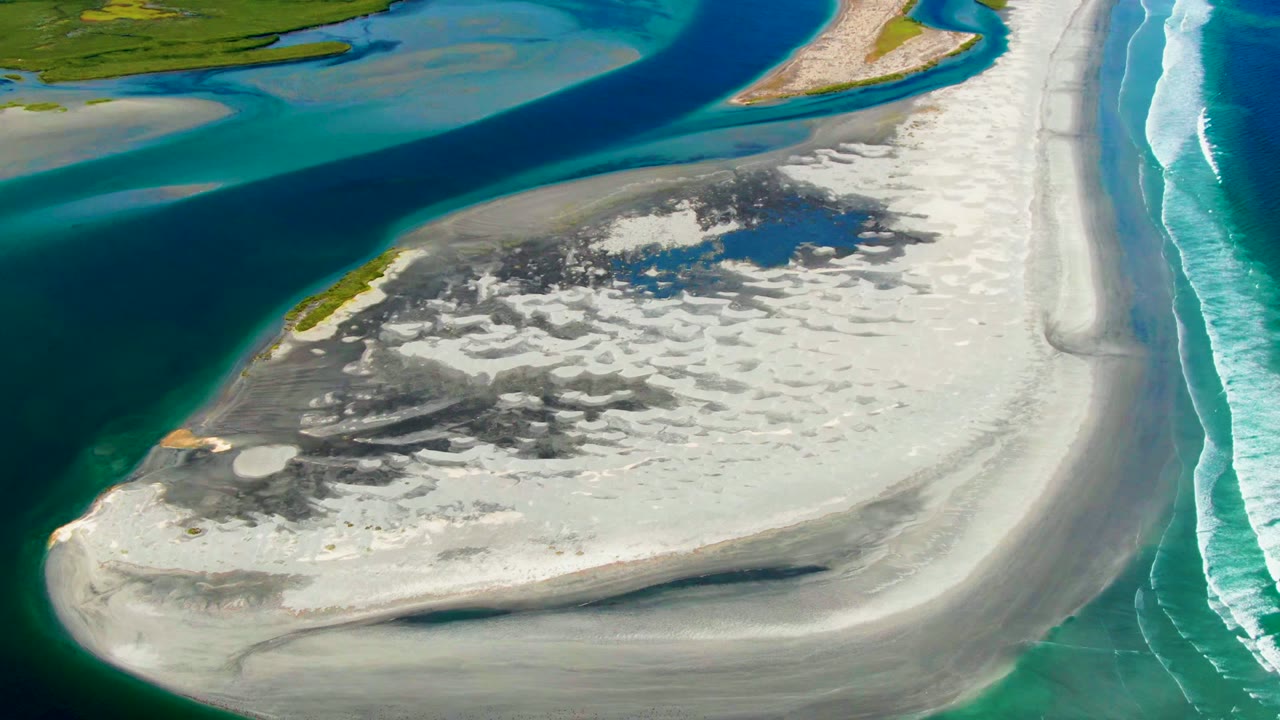 White coastal sandbar with blue river water and surf lines