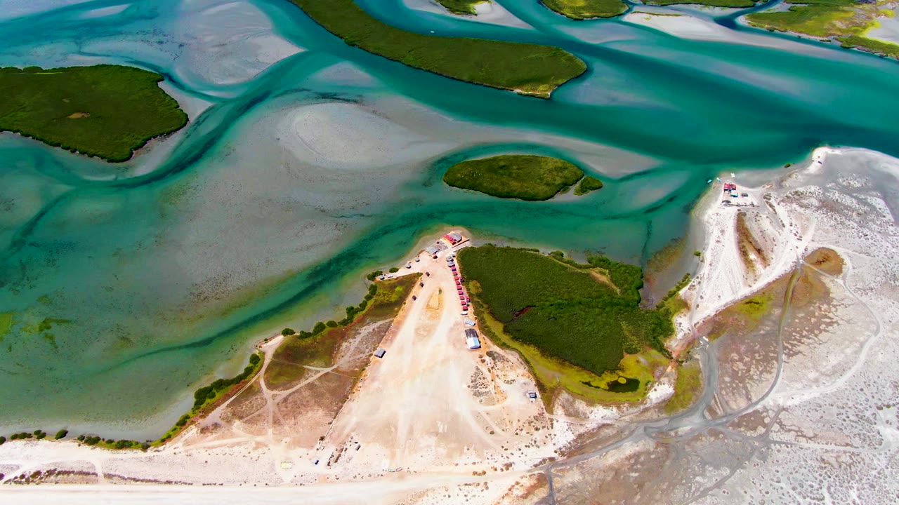 Aerial shoreline with turquoise water, white sand, and green island vegetation.